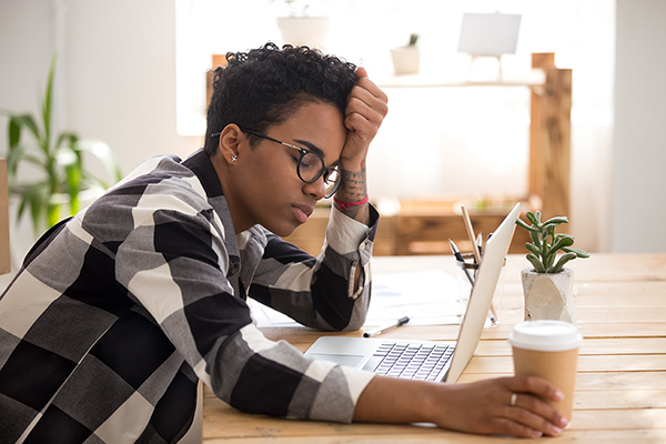 Person falling asleep at their desk clutching coffee