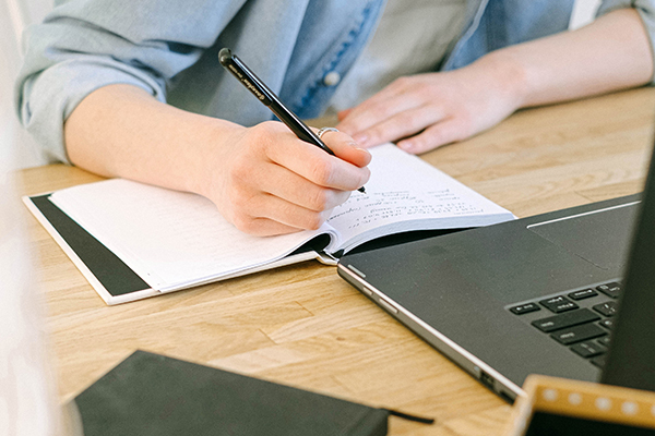 Person writing in notebook next to laptop