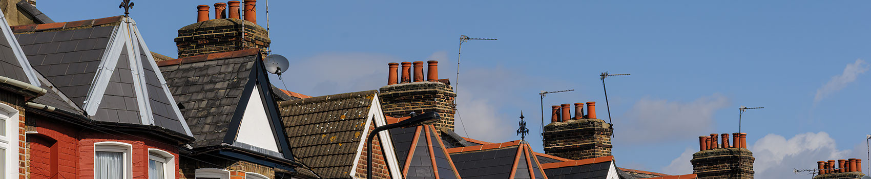 A row of Victorian style rooftops in the UK against a bright blue sky