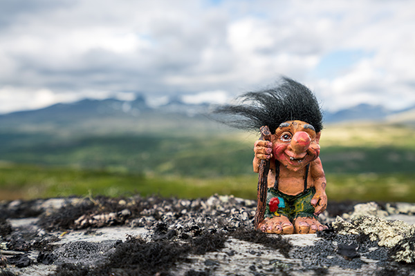 Funny norwegian troll figure with big nose and walking stick outdoors in the mountains. Hair standing up because of windy conditions.