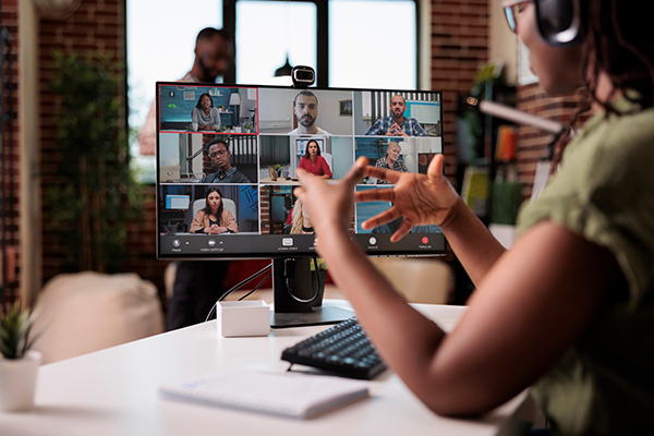 Woman sat at desk gesticulating at a computer screen while talking to a group of people on a work video call