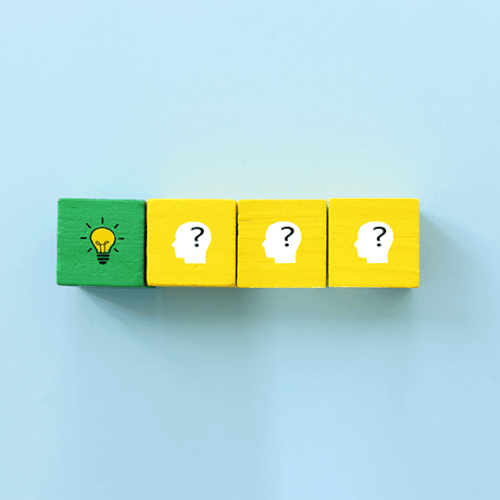 4 wooden cubes in a row, the first is green with a drawing of a lightbulb on it, the other three are identical and show a white outline of a head with a question mark inside