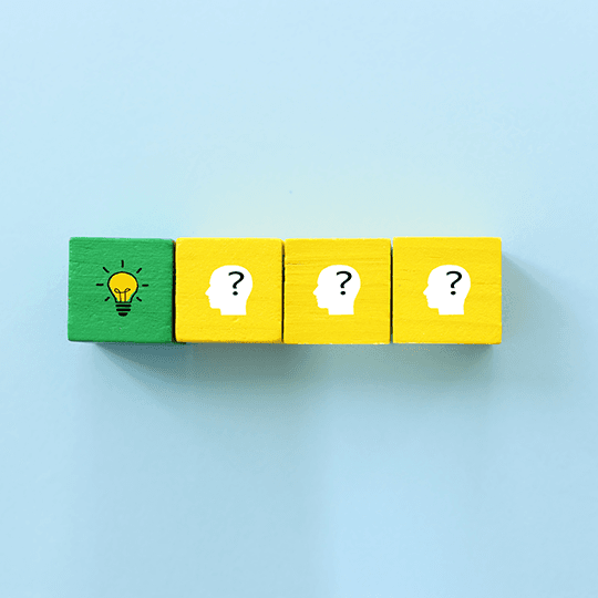 4 wooden cubes in a row, the first is green with a drawing of a lightbulb on it, the other three are identical and show a white outline of a head with a question mark inside
